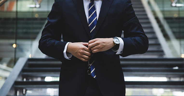 Employee closing up suit blazer walking outside building